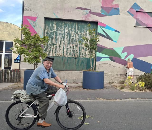 A local cycling by the mural as Brian Lyons carries out his work