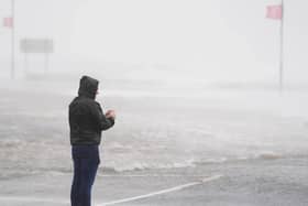 A man looks at a flooded road amid blustery weather